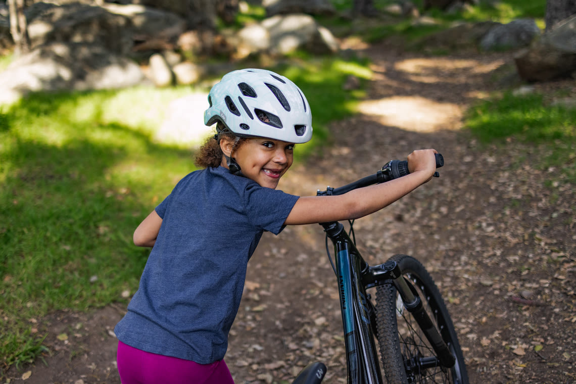 a young girl pushing her mountain bike on a trail