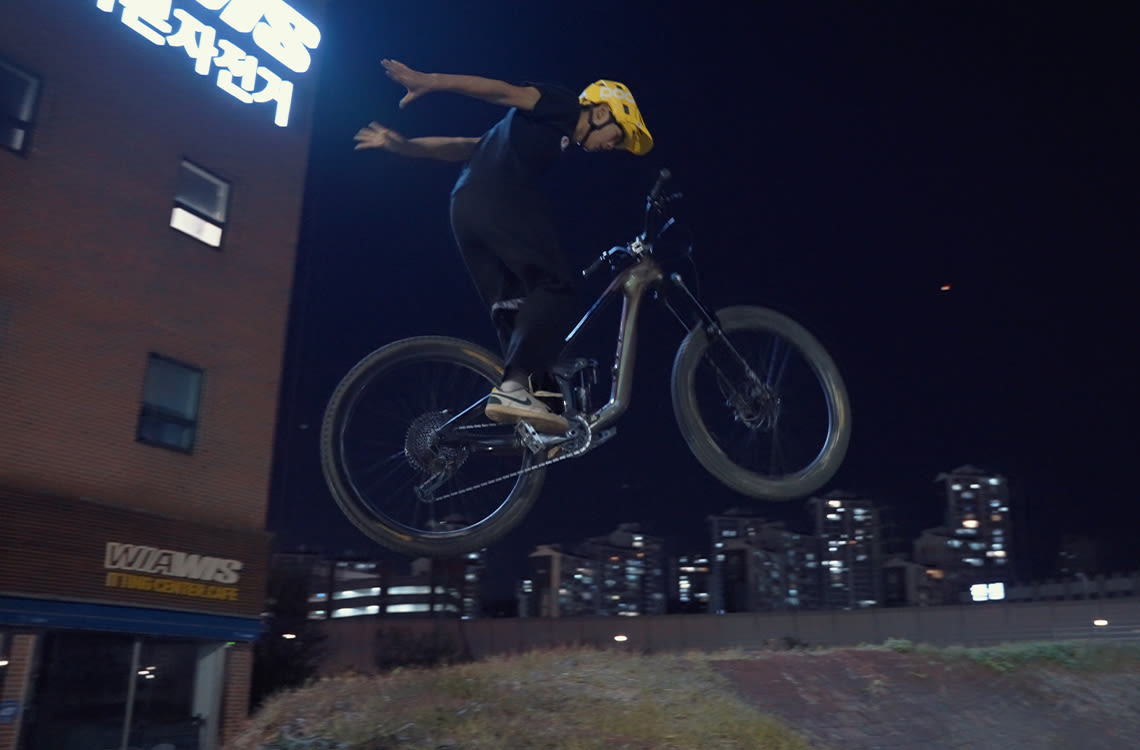 Mountain bikers doing a suicide no-hander out of grass bank.