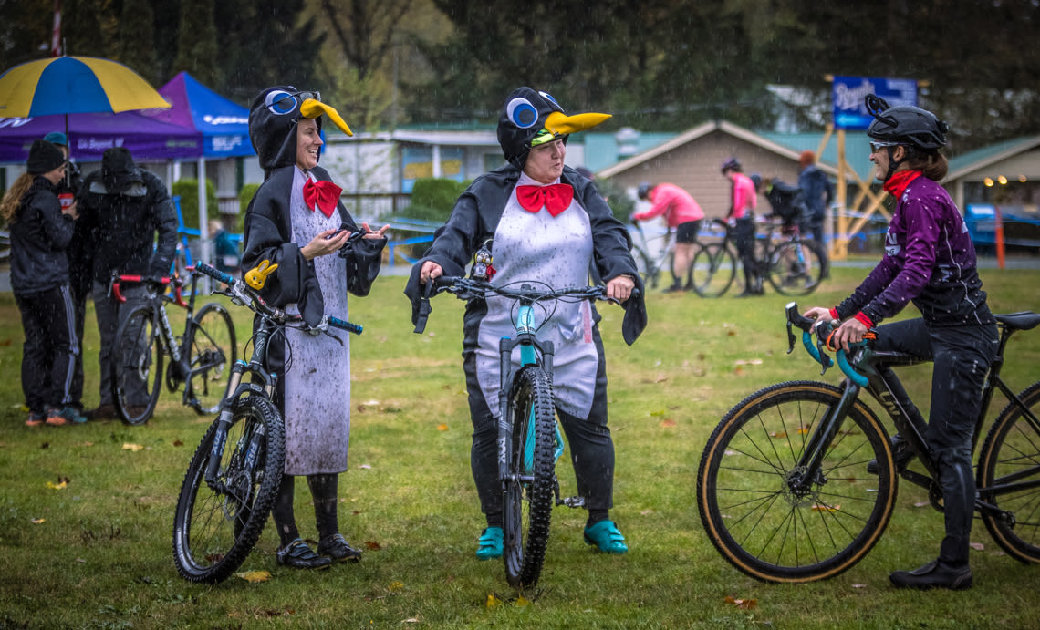 three women at a cyclocross race in costume, two dressed as penguins, one dressed as a butterfly
