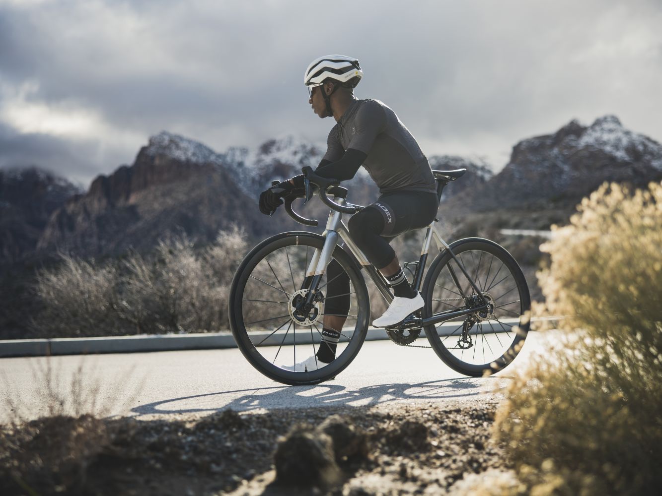 Road cyclist takes a rest to enjoy a snowy mountain backdrop.