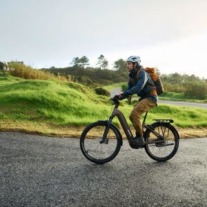 An adventure cyclist rides up a winding paved road through grassy, hill country on a Giant AnyTour X E+.