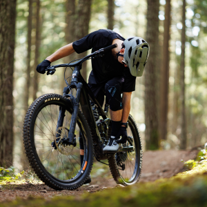 A mountain biker with one foot down on the side of a woodsy trail adjusts their BOA dial on their Giant Shuttle Clip BOA shoes.