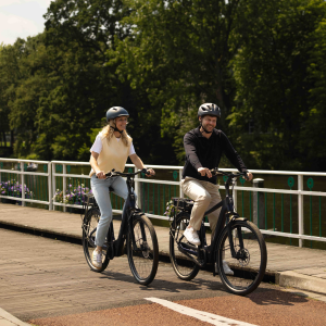 A man and woman riding their Giant Entour E+ city bikes ride a cycle path away from a canal in the city.