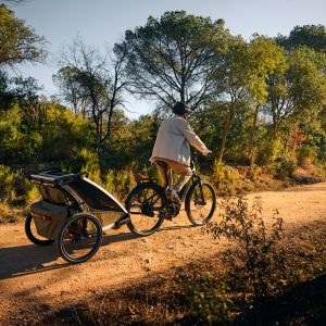 Cyclist rides dirt road on Giant Anytour X E+ pulling trailer.