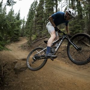 A mountain biker hits a small jump on a forest trail on their Giant Anthem Advanced SL with Giant XCA wheels.
