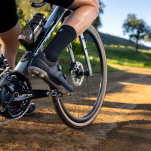 A close up looks at a gravel cyclist wearing Giant Charge gravel shoes resting their foot on the pedal on the side of the trail.