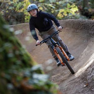 A young rider on a Giant STP 24 rolls through a dirt berm in the forest.