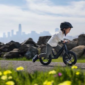 Child riding Giant Pre rCarbon strider bike up bike path with city backdrop.