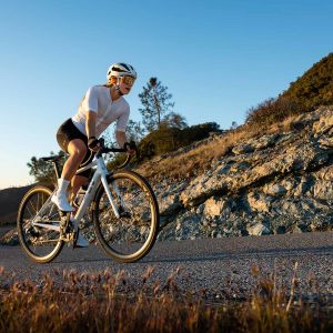 Woman riding a Liv bike up a gravel road wearing Macha shoes.