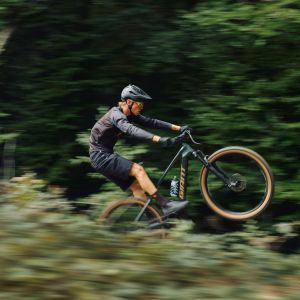 A mountain biker throw in a wheelie as they speed down a forest trail on a Giant Talon E+ mountain bike.