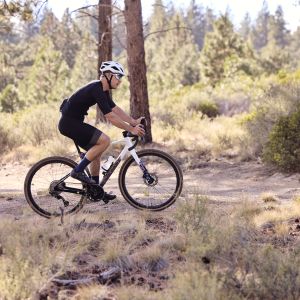 A cyclist rides past on a forested trail riding a Giant Revolt Advanced SE gravel bike.
