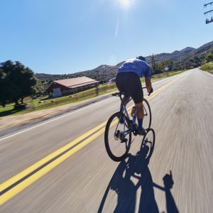Road cyclist sprints down country road on Giant TCR Advanced past a barn.