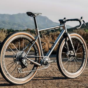 A titanium gravel bike fitted with CADEX Max GXR carbon wheels is staged on a gravel road.
