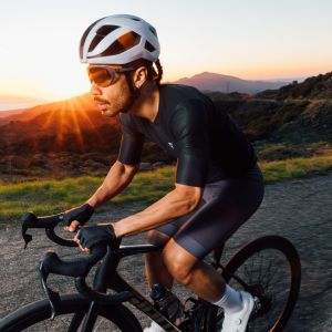 A cyclist on a Giant road bike rides a mountain road at sunset wearing a Giant Rev Pro Helmet.