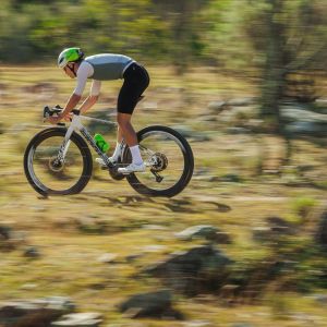 A gravel cyclist rides a Giant Revolt Advanced SL on a sunny trail wearing Giant Charge Pro gravel/XC shoes.