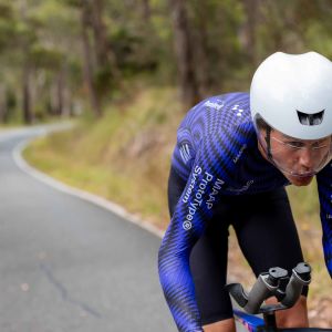 Jayco Alula pro cyclist rides uphill out of the saddle wearing a Giant Rivet Mips Aero helmet.