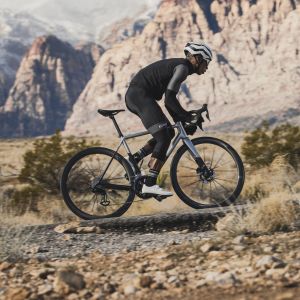 Road cyclist ascends out of the saddle with a snowy mountain-scape in the distance.