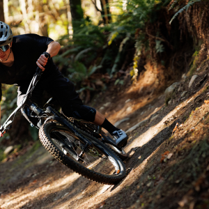 A mountain biker takes a berm on a woodsy trail wearing Giant Shuttle Flat BOA shoes.
