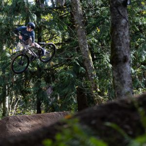 A rider on a Giant STP 26 dirt jumper throws down a huge whip over a forested dirt jump.