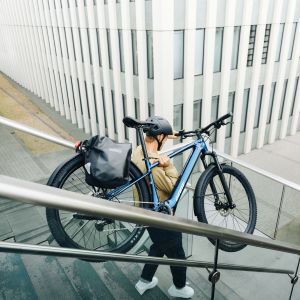 A commuting cyclist walks down some stairs with their Talon E+ EX hardtail bike over their shoulder.