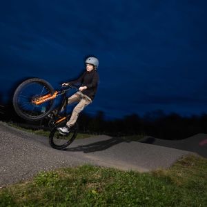 A young rider wheelies over a roller into a berm at an asphalt bike park riding a Giant STP 24 dirt jumper.