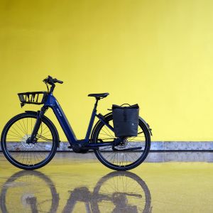 The Giant NewTour E+ from the non-drive side with a pannier in a yellow walled patio.