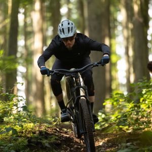 A mountain biker riding a Giant Stance aluminum trail bike charges down a forested trail.