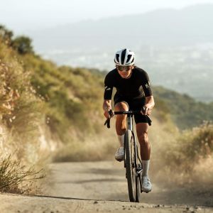 A cyclist rides up a dirt road on a titanium gravel bike with a CADEX Max GXR wheelsystem.