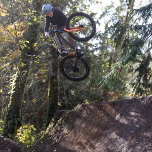 A young rider airs out off a large dirt jump on the woods on a Giant STP 24 dirt jumper.