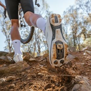 A gravel cyclist wearing Giant Charge Pro gravel/XC shoes runs through a technical section of trail.