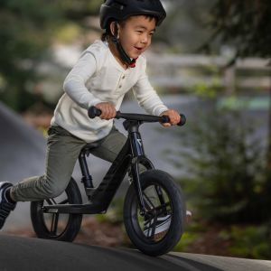 Child riding Giant Pre rCarbon strider bike on forest shrouded pump track.