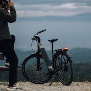 A cyclist with a Giant AnyTour E+ stops at a lookout point to sit on a bench and look out over the city at dusk.