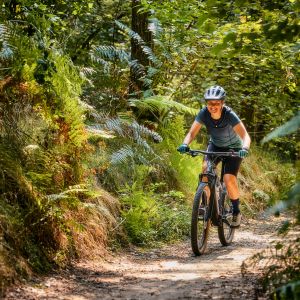 A woman rides a Liv Tempt E+ hardtail mountain bike down a wooded trail.