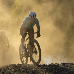 A cyclist rides a Giant Revolt Advanced SL gravel race bike down a dusty road at speed with another rider chasing behind.