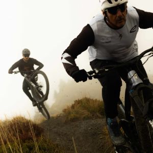 Two mountain bikers on Giant Reign Advanced E+ approach at speed as the rider behind catches air.