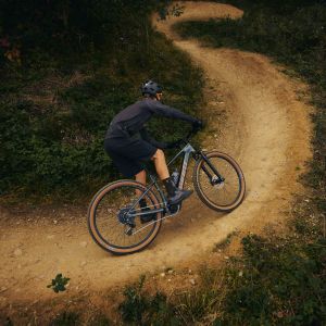A mountain biker exits a berm on a forest trail system on a Giant Talon E+ hardtail mountain bike.
