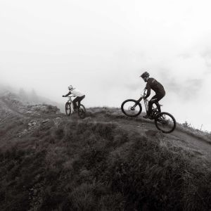Two enduro mountain bikers descend a mountain ridge trail in black and white on Giant Reign Advanced E+.