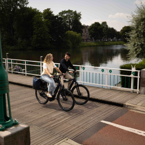 A man and woman ride their Giant Entour E+ city bikes across a pedestrian and bike bridge over a canal. 