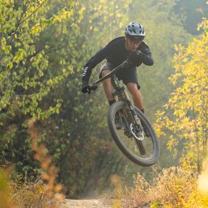 A mountain biker catches air on a mountain trail with fall colors in the background while riding their Giant Anthem X Advanced SL.