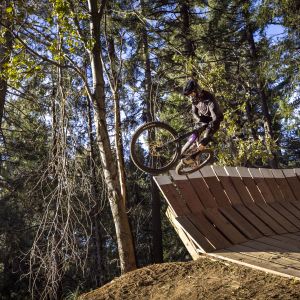 Enduro biker jumping of wall ride at bike park