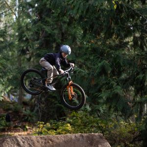 A young rider throws down a hug whip off of a dirt jump in the woods on his Giant STP 24 dirt jumper.
