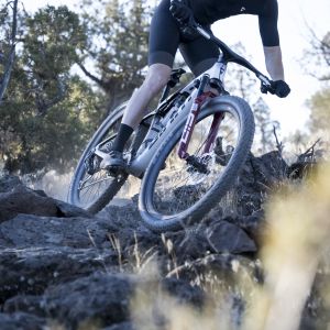 A cross country mountain biker takes a route through a rocky trail riding a Giant Anthem Advanced SL with Giant Contact SLR XC integrated handlebars.