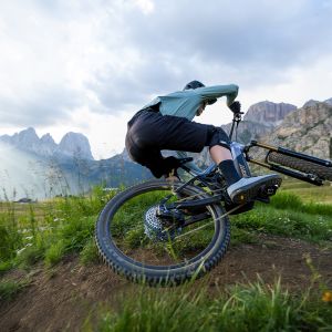 A mountain biker on a Giant TRance Advanced E+ jumps past on a trail with their Giant Contact Switch E+ dropper post in the down position.