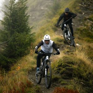 Two mountain bikers on Giant Reign Advanced E+ enduro bikes descend a mountain trail.