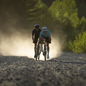 Two cyclists on Giant Revolt Advanced SL gravel bikes ride in single file approaching on a dirt road.