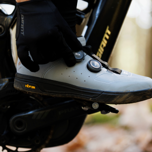 A mountain biker clipped into their pedals adjusts the dial on their Giant Shuttle Clip BOA shoes.