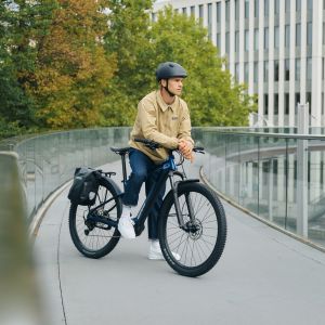 A cyclist rests on a bridge looking out at the city astride their Giant Talon E+ EX hardtail bike with bags and racks.