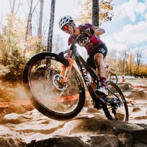 An xc mountain biker races over a rock garden on her iv Pique Advanced SL.