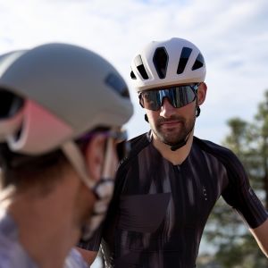 Two cyclists wearing Giant Pursuit helmets converse on the side of the road.