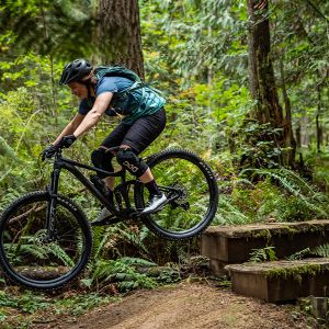A woman riding the new Embolden mountain bike off a wooden drop